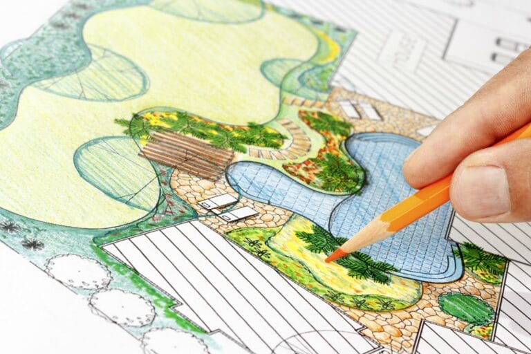 Outdoor Splendor - A hand uses an orange pencil to add color to a detailed landscape design drawing featuring a pool, plants, and patio areas on white paper.