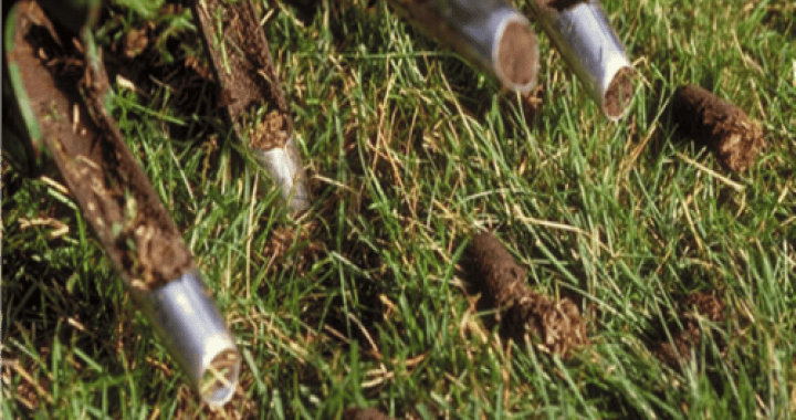 Outdoor Splendor - Close-up of a lawn aerator machine using hollow tines to remove plugs of soil from grassy turf, with soil cores visible on the grass surface.