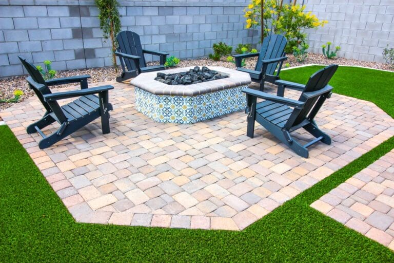 Outdoor Splendor - A backyard patio features four black Adirondack chairs arranged around a decorative stone fire pit on a paved surface, surrounded by artificial green grass and landscaping.